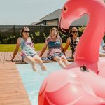 Women enjoying a sunny day by the pool with an inflatable flamingo, epitomizing summer fun.
