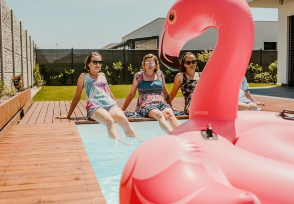Women enjoying a sunny day by the pool with an inflatable flamingo, epitomizing summer fun.