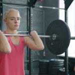strong young woman doing barbell squats training with instructor in gym. Sports people, active lifestyle and bodybuilding concept.