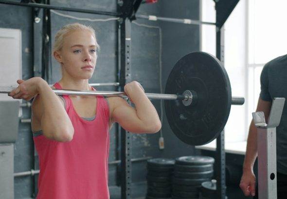 strong young woman doing barbell squats training with instructor in gym. Sports people, active lifestyle and bodybuilding concept.